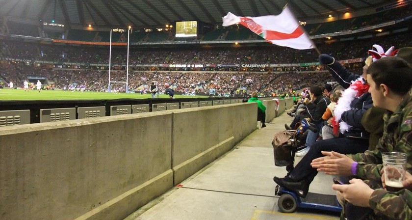 A view of Twickenham Stadium form the front row with somebody waving an England flag.
