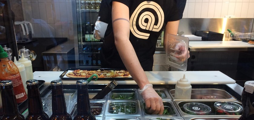 A staff member at @pizza making pizza at the counter