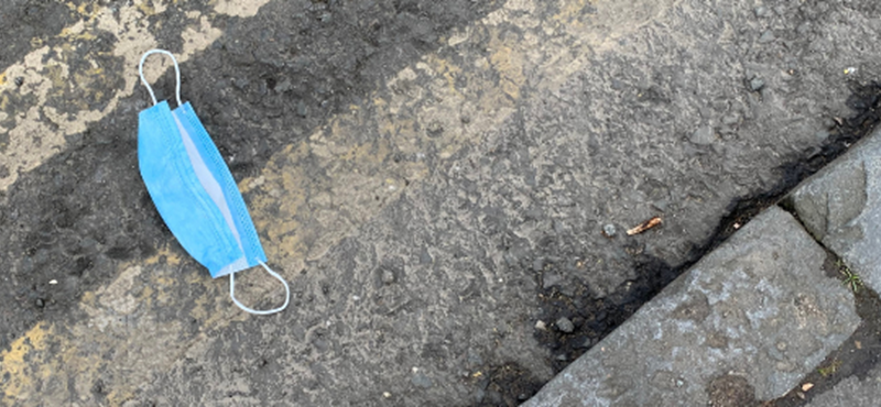 Image of a disposable face mask lying at the isde of the road.