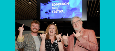 Photo of Jamie Rea, Solar Bear; Shona McCarthy, Edinburgh Fringe Festival CEO, Philip Gerrard, Deaf Action CEO using sign language underneath a large screen with Edinburgh Deaf Festival graphic displayed