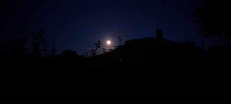 A night sky with a small white dot that is the moon giving a glow