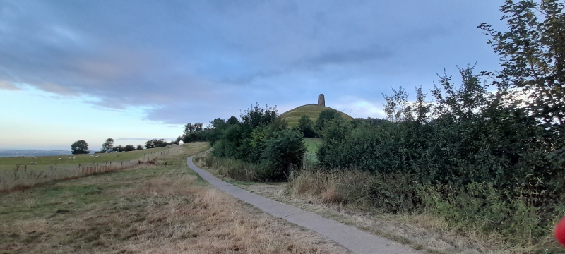 A view up a grassy hill with a path leading up to a stone tower in the far distance