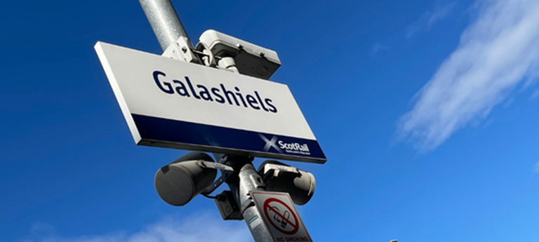Train station signage saying Galashiels against a blue sky