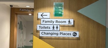 A photograph of signage pointing to family room, toilet and Changing Places toilet