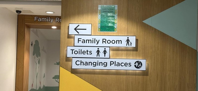 A photograph of signage pointing to family room, toilet and Changing Places toilet