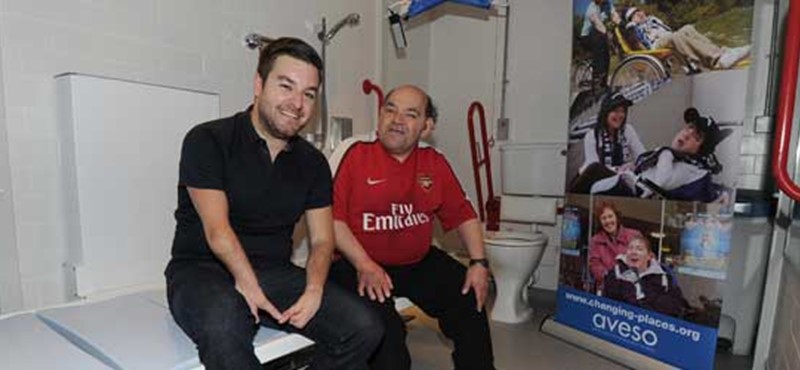 A photo of two people inside a Changing Places Toilet. 