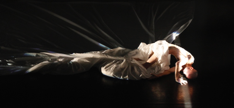 Photo of Marc Brew dancing with white sheets against a black backdrop.