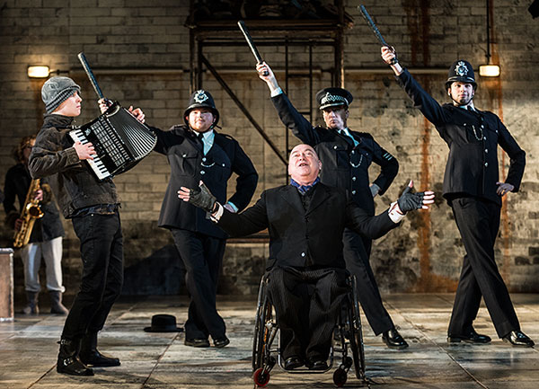 Photo of wheelchair user singing centre stage with four policemen behind him