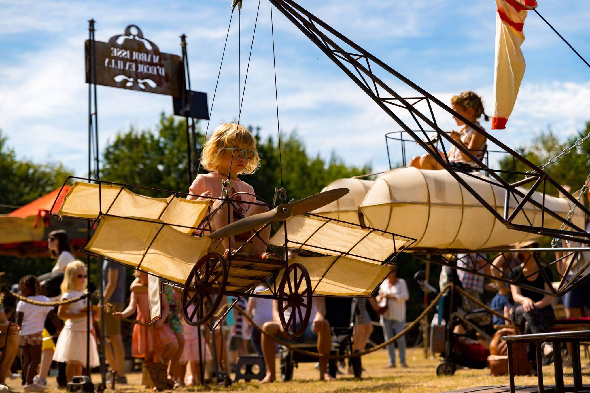 Children sit in a swing crafted to look like a plane at a festival outdoors