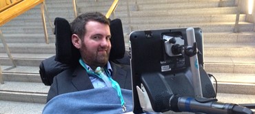A photograh of Euan in front of steps at the Scottish Parliament