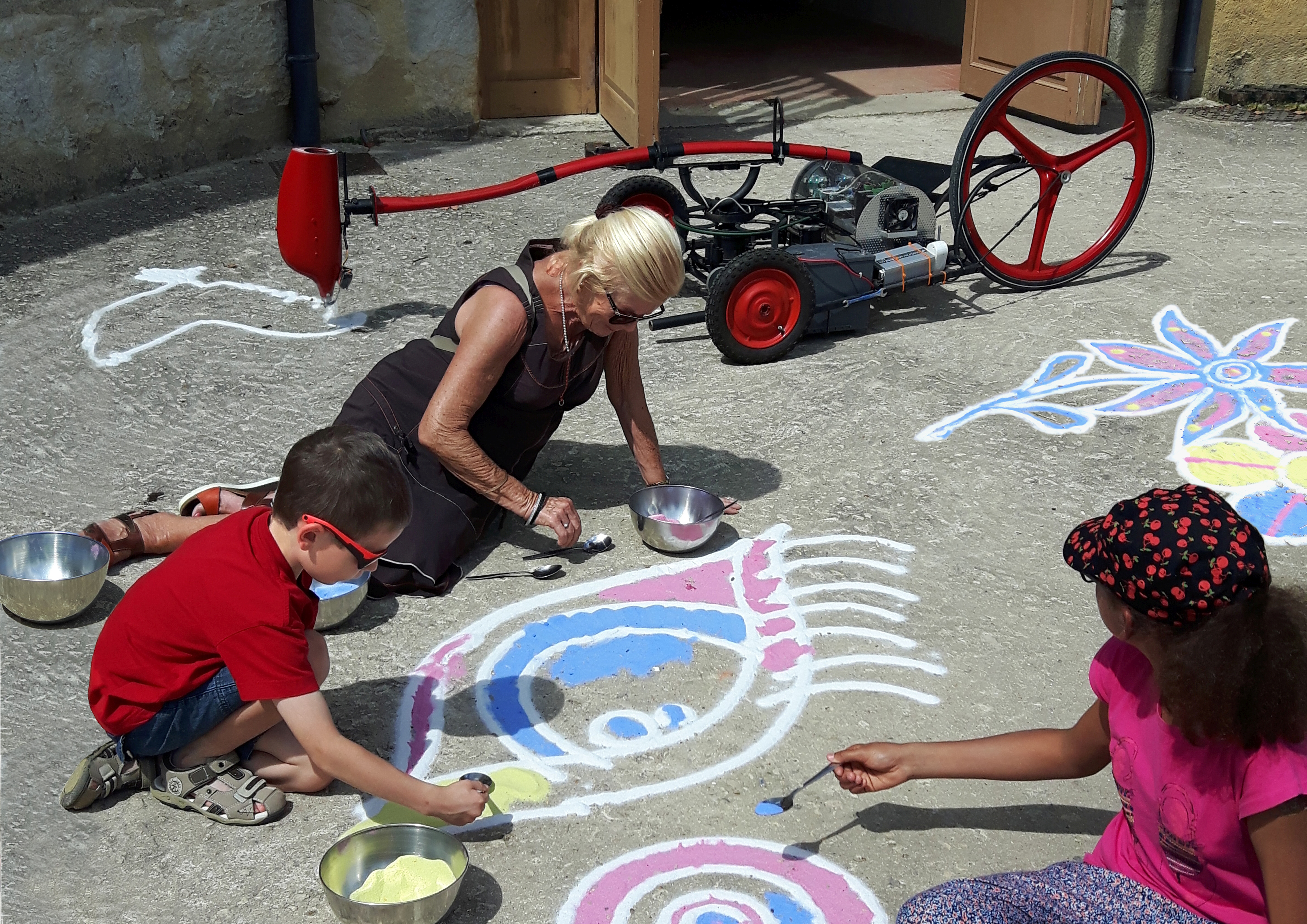A woman and two children draw on a pavement with colourful chalk