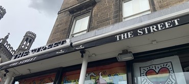 A photograph of the exterior of The Street venue named in the blog post, with a rainbow heart picture in the window with other rainbow coloured pictures just seen