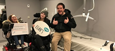 A photograph of three Euan's Guide staff and ambassadors smiling to camera. They are in a Changing Places toilet with Euan's Guide logo banners
