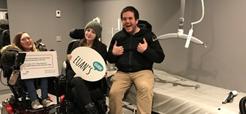 A photograph of three Euan's Guide staff and ambassadors smiling to camera. They are in a Changing Places toilet with Euan's Guide logo banners