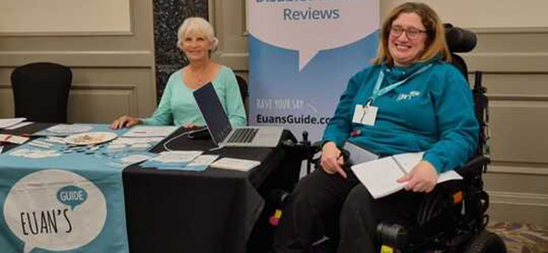 Two women at the Euan's Guide exhibition stand with Euan's Guide branded pop up banner and table cloth