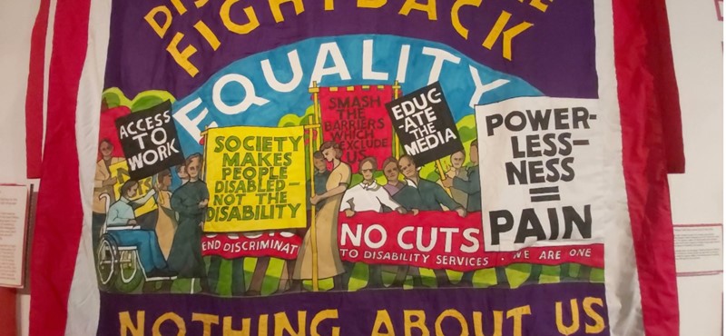 A photo of a fabric artwork with the text 'disabled people fight back' 'powerless-ness = pain' 'nothing about us without us' and a picture of people protesting for disability rights