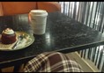 Red velvet cupcake and a coffee cup on a black coffee table in the bar area of the BFI Southbank. Showing an orange velvet armchair and a black string curtain to the right. A person's trouser leg can be seen at the bottom of the image