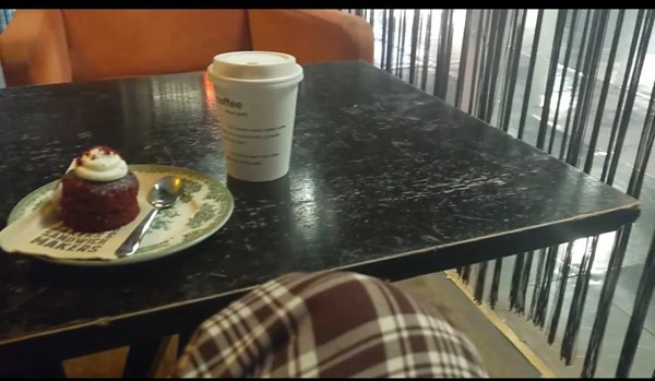 Red velvet cupcake and a coffee cup on a black coffee table in the bar area of the BFI Southbank. Showing an orange velvet armchair and a black string curtain to the right. A person's trouser leg can be seen at the bottom of the image