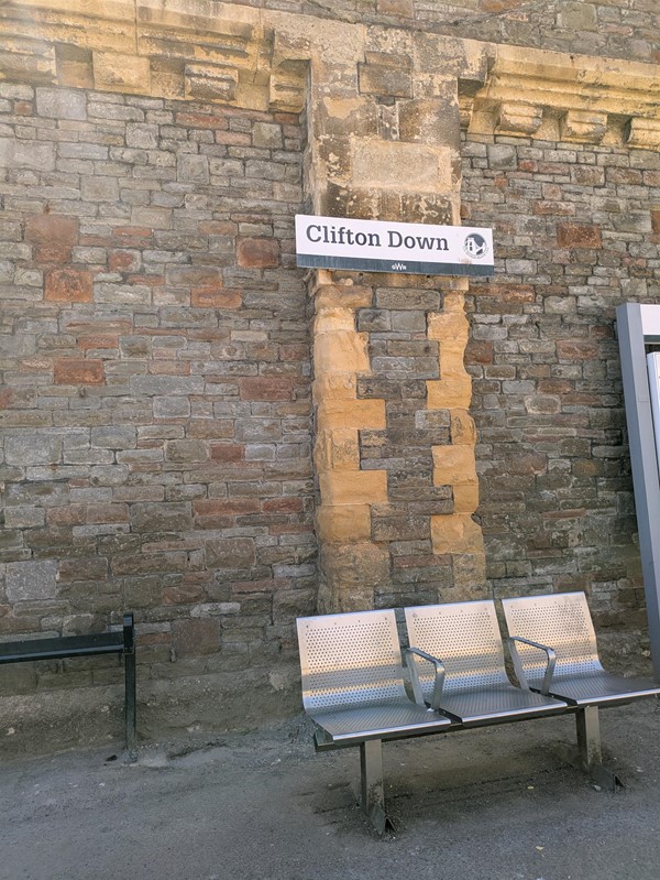 Image of metal seats on platform below a sign marked Clifton Down