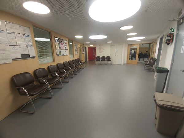 Chairs lined up on the left hand wall of a corridor leading to a door