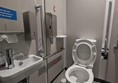 Image of the accessible toilet showing the toilet, grab rails, red cord, paper towel dispenser and the sink