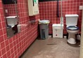 Image taken from the opening of the bathroom. View shows the mirror and baby change on one side of the toilet and the bins in the corner.