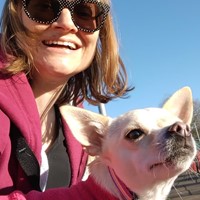 Woman in sunglasses with small dog. Both wearing pink.