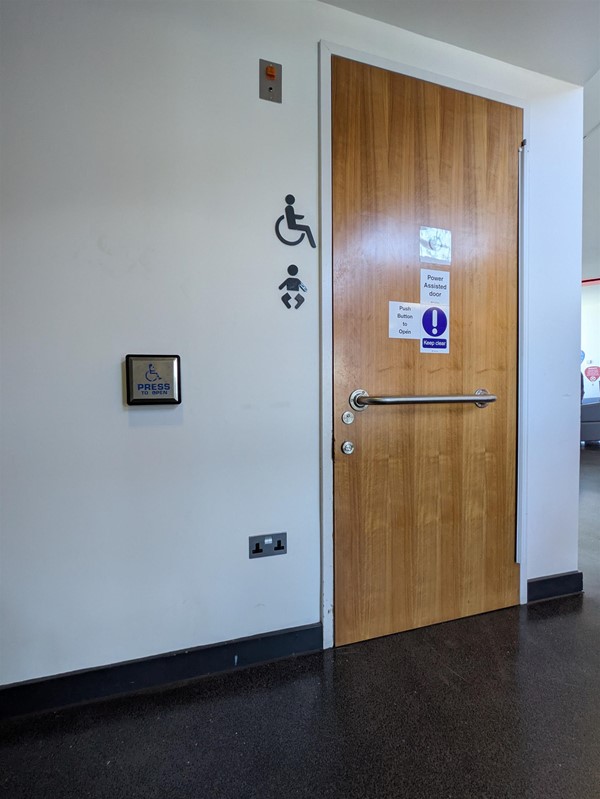 Image of accessible toilet door from the outside with horizontal grab rail and a button to open the door
