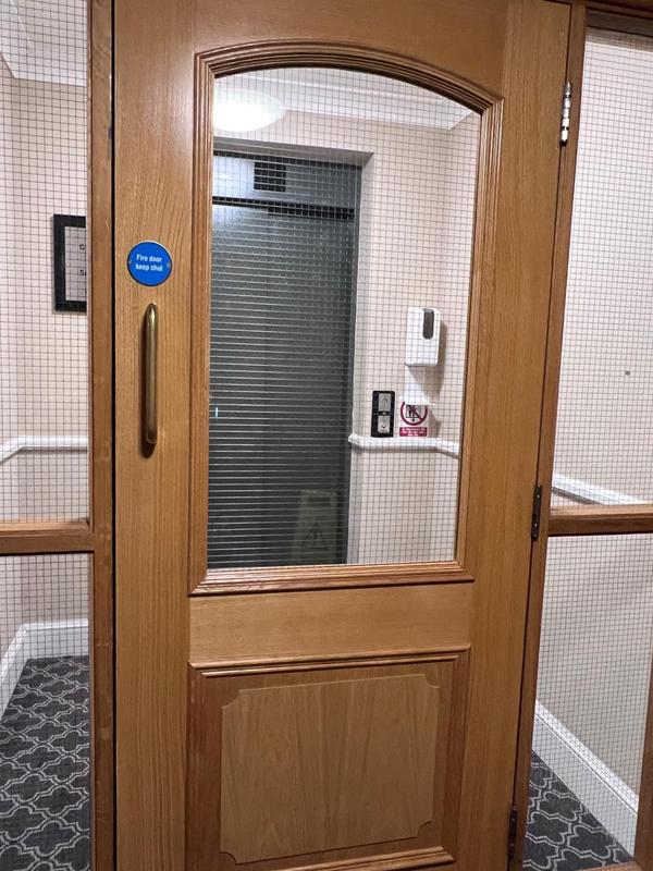 Access to the lifts was through a door that was too heavy to open independently. Photo shows a lift with a door and glass frame to get to it.