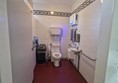 A wider view of the accessible toilet showing three grab rails on the right-hand wall and a clearer picture of the available floor space.