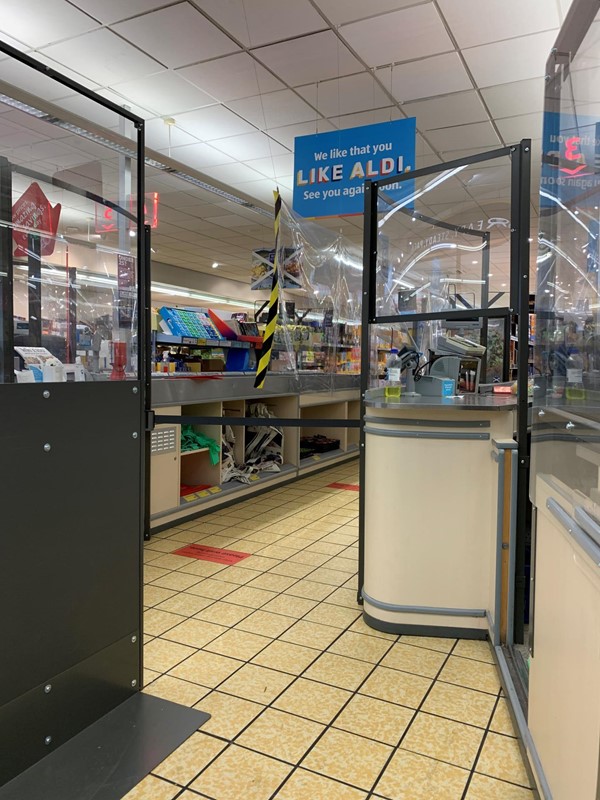 Image of dividers at the tills of Aldi. There are also red social distancing stickers on the floor.