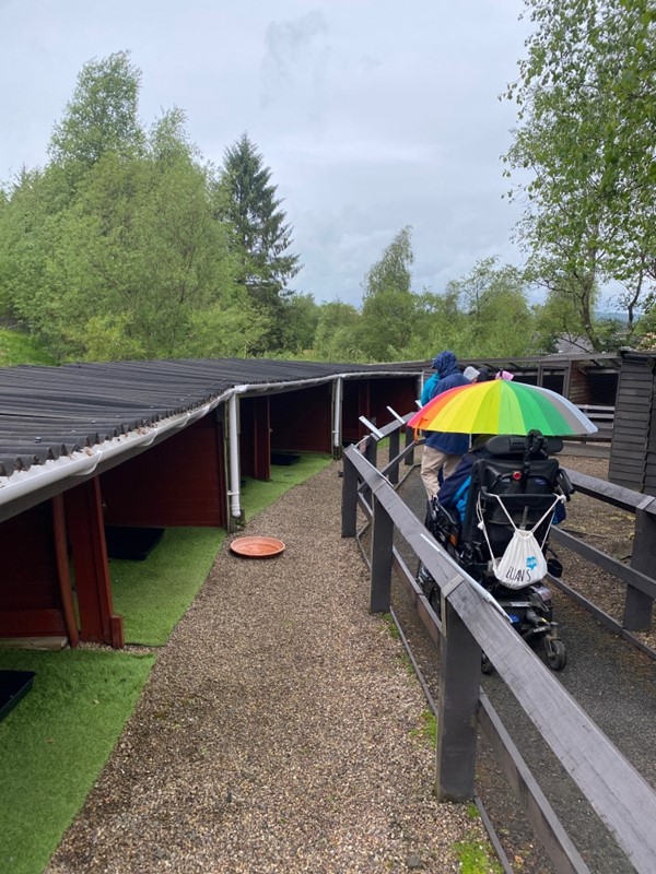 Image of a wheelchair user with an umbrella going down a pathway