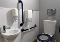 Image of  accessible toilet with contrasting seat, rails and small sink with lever-style tap