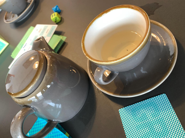 Good games and drinks. Pic shows grey teapot with matching cup abs saucer. Cards and dice from the game Chameleon are scattered around.