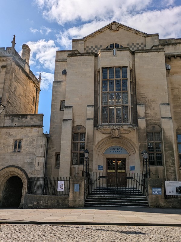 Image of the main entrance to the library. A sandstone building with steps and a set of brown double doors.