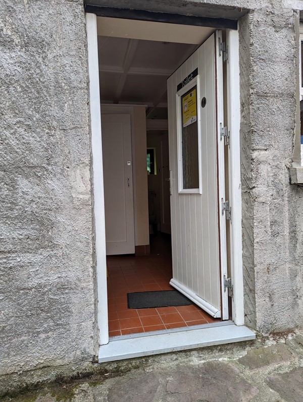 The loo, featuring a mighty step!

A white door set in a grey stone wall. Inside is a toilet with cubicles and a terracotta tiled floor . The accessible cubical is opposite the door.