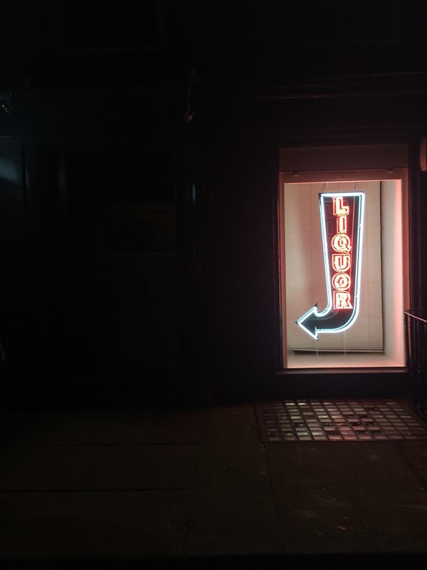 Front of the bar illuminated only by their liquor sign.
