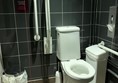 View of toilet from door showing red cord, handrails, bins and toilet roll dispenser