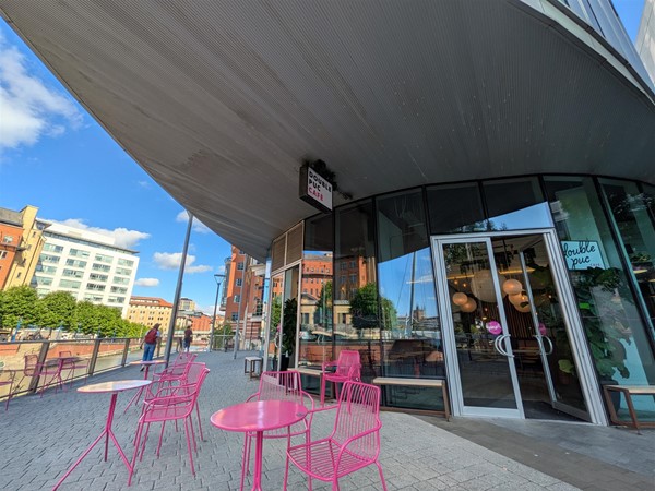 Image of pink metal seats and pink tables outside of the café