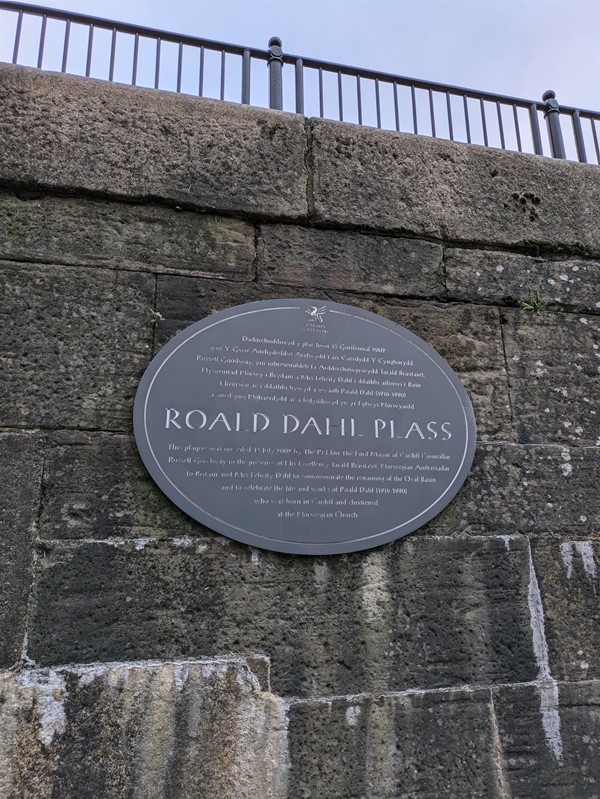 Image of a grey plaque on a brick wall with the writing Roald Dahl Plass