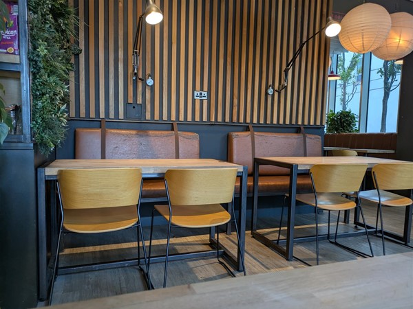 Image of yellow wooden seats at a table, there are brown leather bench seats at the back