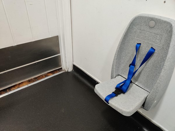 Fold-down seat cannot be fixed in the up position, an obstruction for wheelchair users entering the toilet vestibule area