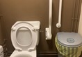 View of accessible toilet from door showing two handrails on left hand side of toilet.