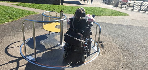 Picture of a Claire in her wheelchair on the round-a-bout