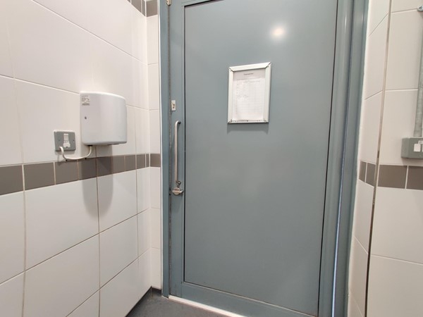 The toilet door lacks a grabrail on the inside, making it impossible for a wheelchair user to close the door from the inside. The mechanical hand-dryer is positioned too high for a wheelchair user to use it.