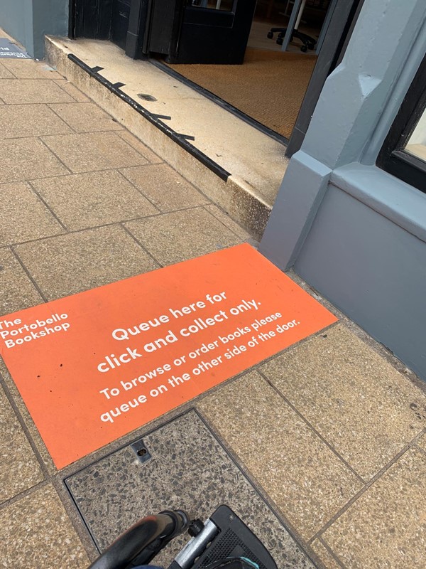 Social distancing sticker on the floor outside. It reads “The Portobello Bookshop. Queue here for click and collect only. To browse or order books please queue on the other side of the door.”