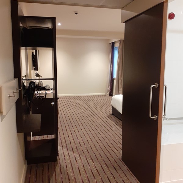 The entrance to the accessable hotel room. The bathroom door is on the right and the wardrobe is on the left. Then the room opens out with the bed on the right and plenty of open space ahead.