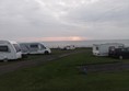 Beuatiful view out to sea, with sunrise. Path through the site is tarmac with grass either side and then gravel pitches.