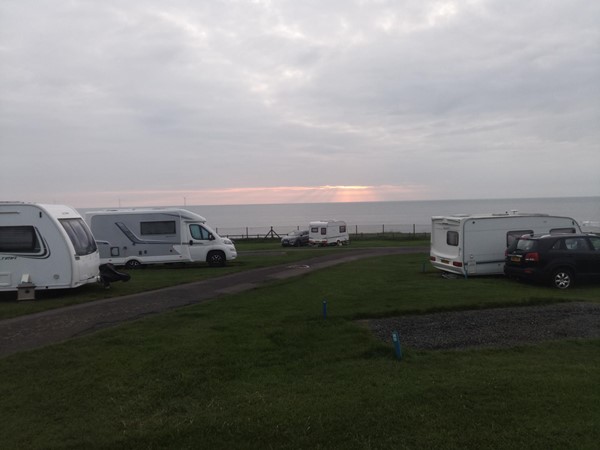 Beuatiful view out to sea, with sunrise. Path through the site is tarmac with grass either side and then gravel pitches.