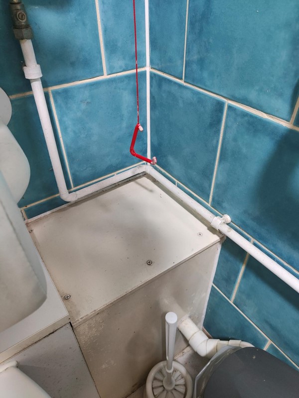 red emergency cord in the awkward corner of the toilet and  not accessible if a fall was to occur